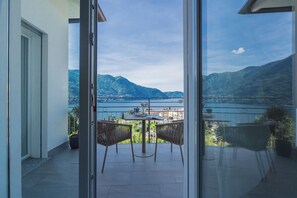 A balcony with a table and chairs, a view of a lake and mountains, and a door leading to the interior. - Villa Caterina–Smeraldo Lake View Terrace (Moltrasio)