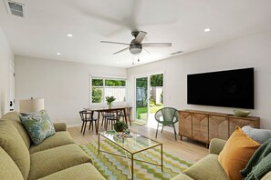 Ein Wohnzimmer mit Sofa, Couchtisch, Fernseher und einem Essbereich mit Stühlen und Tisch.