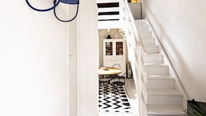 Una escalera conduce a un comedor con un tapete de diseño blanco y negro, armarios blancos y una pequeña mesa con sillas.