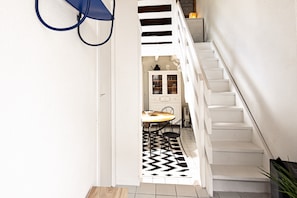 Una escalera conduce a un comedor con un tapete de diseño blanco y negro, armarios blancos y una pequeña mesa con sillas.