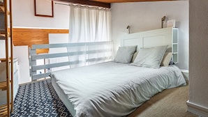 Un dormitorio con una cama litera, una mesita de noche, una lámpara y una ventana con cortinas.