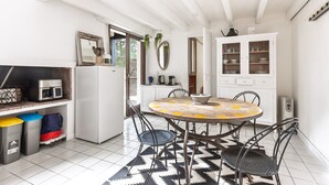 Una cocina con una mesa redonda, sillas, un refrigerador, armarios y un microondas.
