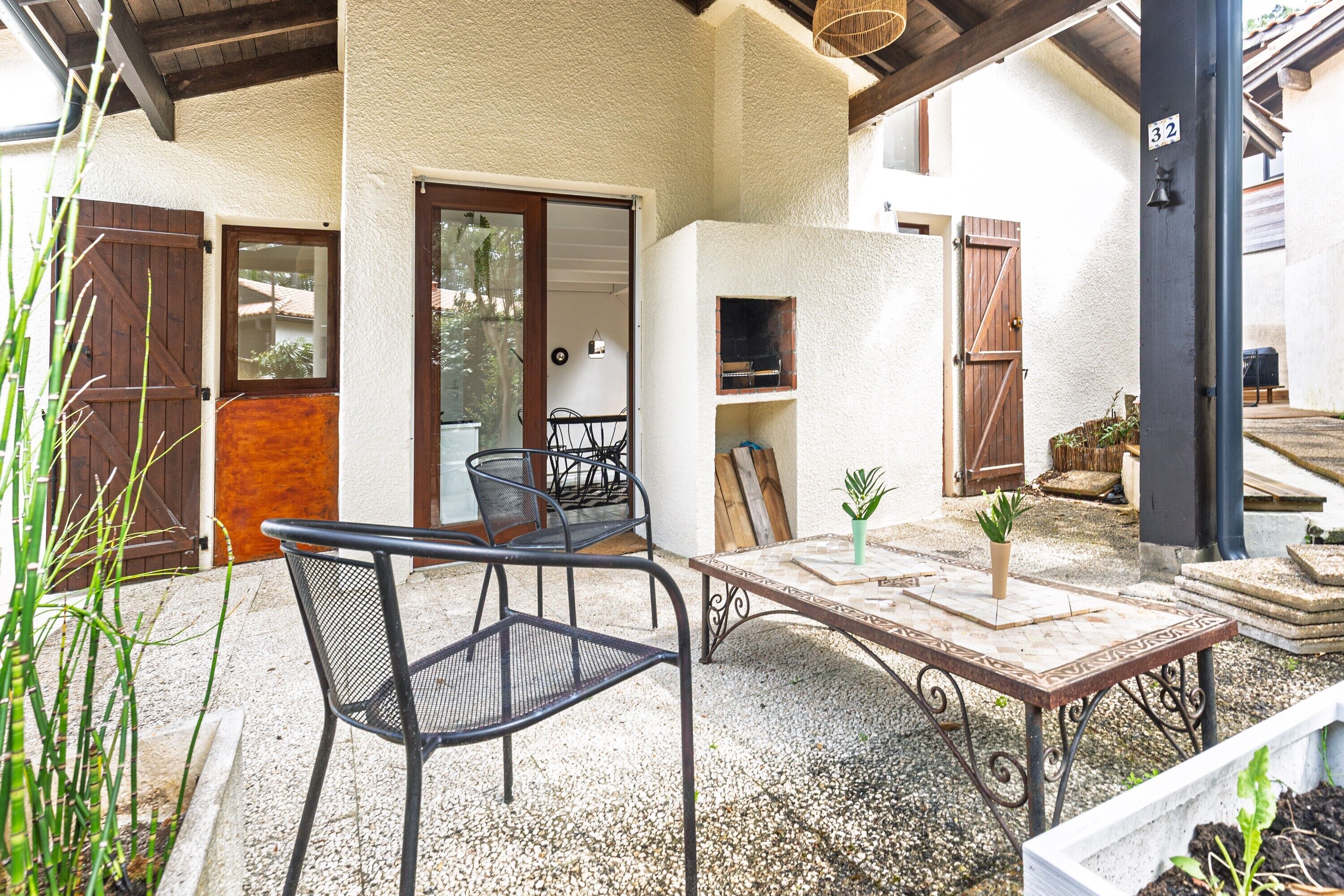 Une terrasse extérieure avec une table et des chaises, un pot de fleurs et un espace barbecue.