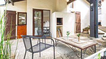 Une terrasse extérieure avec une table et des chaises, un pot de fleurs et un espace barbecue.