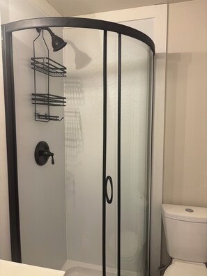Eine gläserne Dusche mit schwarzem Rahmen, schwarzem Türgriff und einem Handtuchhalter.