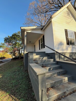Ein Haus mit Veranda und einer Treppe aus Beton, die zum Eingang führt, unter einem wolkenlosen Himmel.