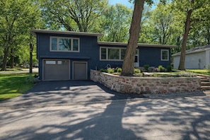 A two-story house with a stone retaining wall, a garage, and a well-maintained lawn. - Okoboji Lake House (Okoboji)