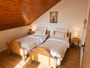 Ein Schlafzimmer mit zwei Holzbetten, einer schrägen Decke und einem Bild eines Rehs an der Wand.