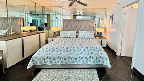 Ein Schlafzimmer mit einem Bett, Nachttischen, einem Spiegel und einem Deckenventilator.