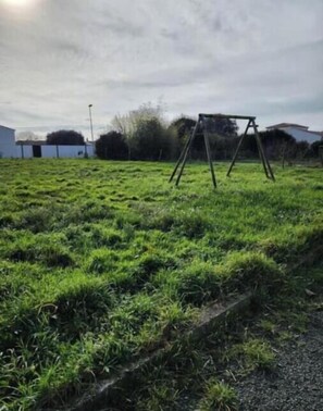 A grassy field with a swing set and a building in the background. - Farm cottage with sea view - Charm & Nature near La Rochelle (Marsilly)