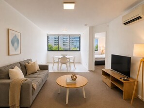 Moderni olohuone, jossa on sohva, sohvapöytä, televisio ja ruokailutila tuoleineen.
