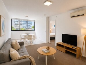 A modern living room with a sofa, a round coffee table, a TV on a wooden stand, and a dining area with a table and chairs. - Bright Bowen Hills 2BR Escape Near CBD (Brisbane)