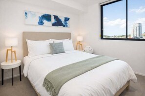 A hotel room with a bed, two bedside tables, a nightstand, a window with a city view, and abstract wall art. - Bright Bowen Hills 2BR Escape Near CBD (Brisbane)