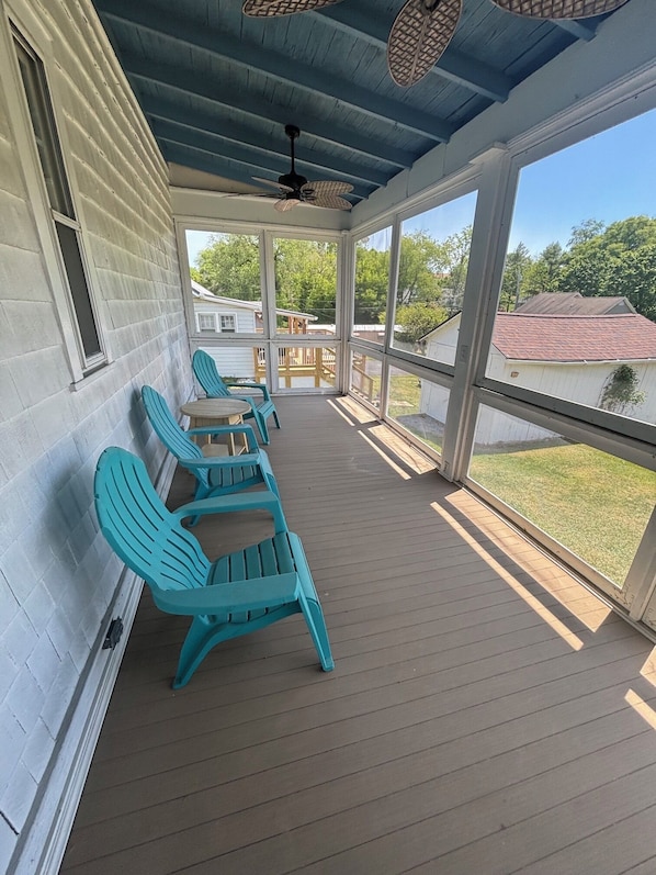 Eine überdachte Veranda mit blauen Adirondack-Stühlen, einem Deckenventilator und Blick auf die Nachbarhäuser.
