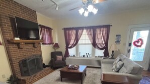 A living room with a fireplace, a ceiling fan, a television mounted on a brick wall, and a sofa. - Spacious 5-bedroom house in serene Fincastle with AC (Fincastle)