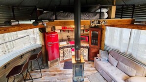 A rustic interior with a wooden bench, a red appliance, a wooden cabinet, and a sofa. - Bin There Treehouse - A Grain Bin treehouse! (Washington County)