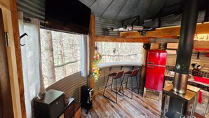 A rustic interior with a wooden ceiling, a red refrigerator, a stove, and a window with a view of trees. - Bin There Treehouse - A Grain Bin treehouse! (Washington County)