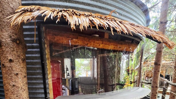 A rustic, cylindrical structure with a thatched roof, a small seating area, and a view of the surrounding forest. - Bin There Treehouse - A Grain Bin treehouse! (Washington County)