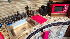 A kitchen with a stone countertop, a sink, a red microwave, and a wall clock. - Bin There Treehouse - A Grain Bin treehouse! (Washington County)