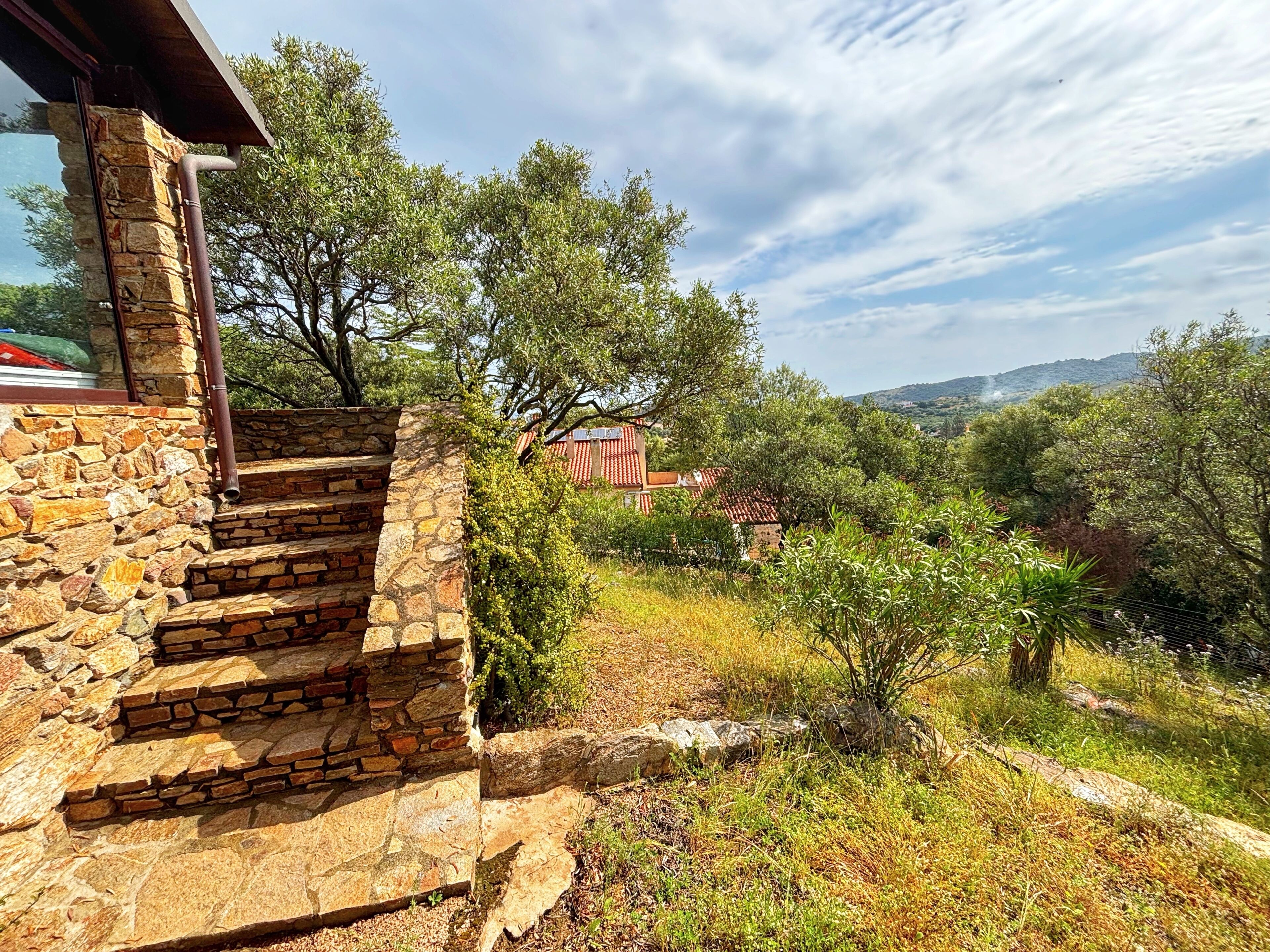 A stone staircase leading to a building with a view of a red-roofed structure and surrounding trees.
