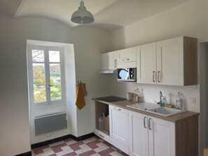 Eine Küche mit weißen Schränken, einer Mikrowelle, einem Spülbecken und einem Fenster mit Blick auf Bäume.