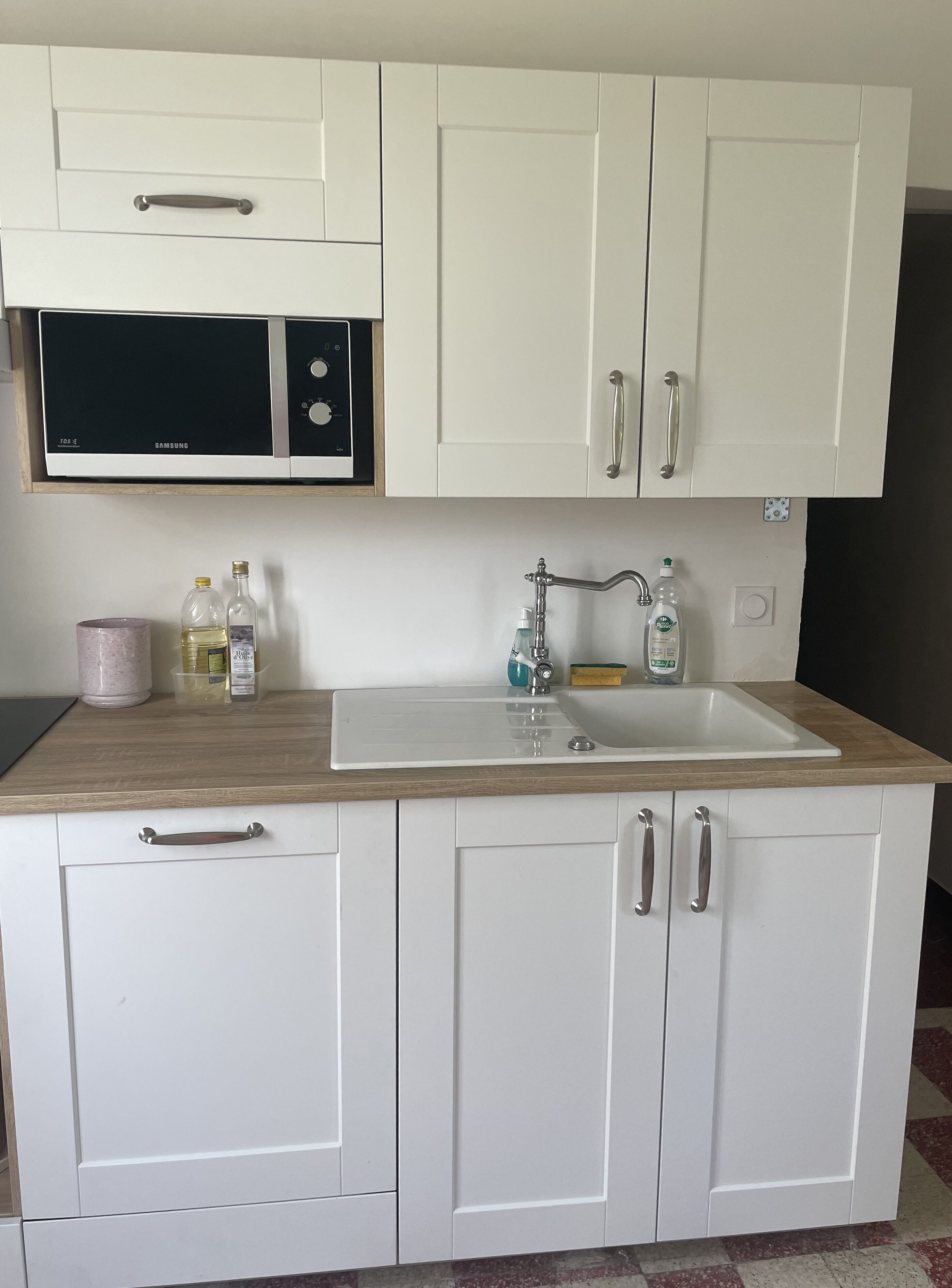 A kitchen with white cabinets, a microwave, a sink with a faucet, and various kitchen items on the countertop.