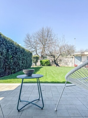 A patio with a round table and metal chairs, a hedge, and a lawn with trees. - Villarzilla - beautiful villa (Roma)
