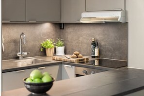 A modern kitchen with a built-in sink, a stove, and a countertop. There are potted plants, a cutting board with bread, and bottles on the counter. - Modern 2-bedroom apartment in in the Heart of Oslo (Oslo)
