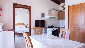 A room with a bed, a dining table with chairs, a kitchen area with cabinets and appliances, and a television. - Peristeri 1 Bd Apt w Balcony and View (Peristeri)