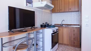 A compact kitchen with a stove, oven, sink, and a flat-screen TV on a wooden table. - Peristeri 1 Bd Apt w Balcony and View (Peristeri)