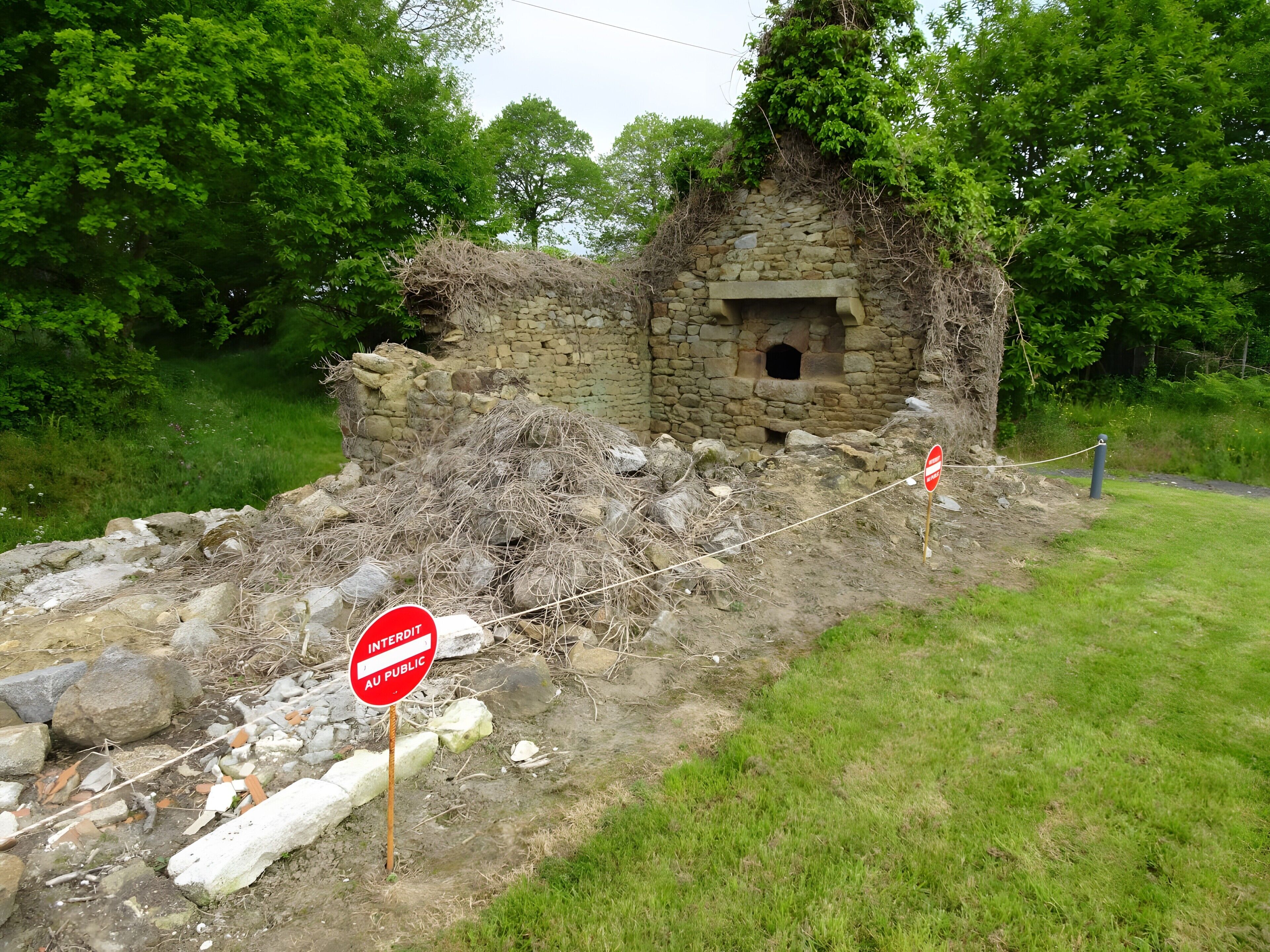 Une structure en pierre dotée d’une petite ouverture, entourée d’une végétation luxuriante et d’un panneau indiquant « accès interdit ».
