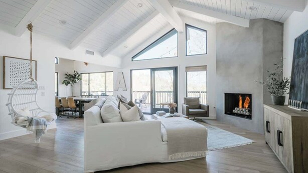 A spacious living room with a high ceiling, large windows, a fireplace, and a dining area.