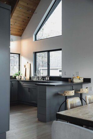 A modern kitchen with a large island, dark cabinetry, and a wooden ceiling. - The Boujee Basecamp, by Tag Home Design (Lake Arrowhead)