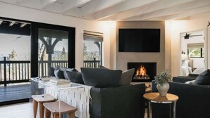 A modern living room with a fireplace, a sofa set, and a view through large windows.
