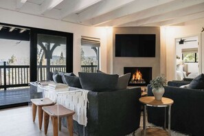 A modern living room with a fireplace, a sofa set, and a view through large windows. - The Boujee Basecamp, by Tag Home Design (Lake Arrowhead)