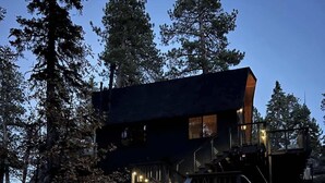Un chalet à plusieurs niveaux, doté d’un escalier extérieur, entouré d’arbres et de rochers.