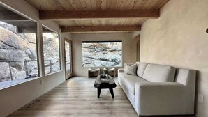 Un vaste salon doté d’un plafond en bois, d’un canapé, d’une table basse et de grandes fenêtres offrant une vue sur un paysage rocheux.