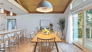 Ein Essbereich mit Holztisch und Stühlen, einer Pendelleuchte und Blick durch große Fenster.