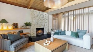 Ein Wohnzimmer mit Kamin aus Stein, zwei Sofas, einem Couchtisch und einer Pendelleuchte.