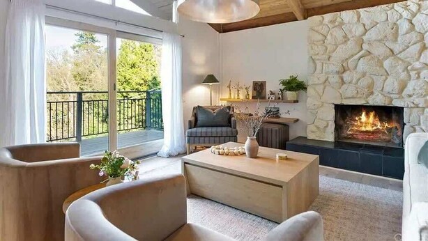 Ein modernes Wohnzimmer mit Kamin aus Stein, einem großen Fenster mit Vorhängen und einem Balkon.