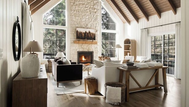 Un salón espacioso con chimenea de piedra, ventanas amplias y un alto techo de madera.