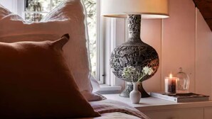 Een slaapkamer met een bed, een lamp, een raam met uitzicht en een nachtkastje met een kaars.