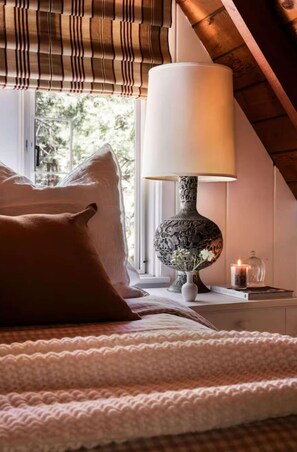Ein Schlafzimmer mit Bett, Lampe, Fenster mit Blick und Nachttisch mit Kerze.