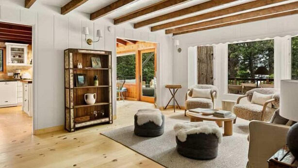 Een ruime woonkamer met houten balken, een open haard en uitzicht op het landschap.