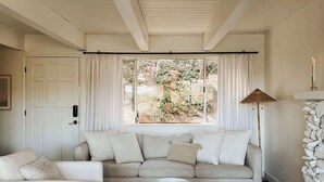 En moderne stue med sofa, to lænestole, sofabord og udsigt til grøn vegetation gennem store vinduer.