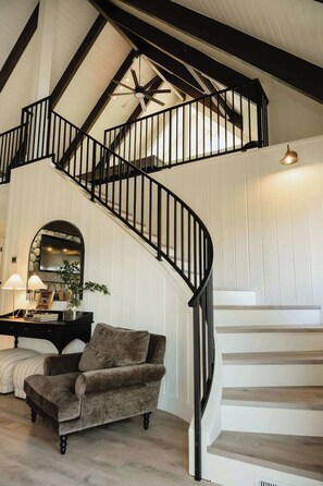 A spiral staircase with black railings, a plush armchair, and a stone fireplace. - @grizzlymountainhouse-lake access/firepit/games (Lake Arrowhead)