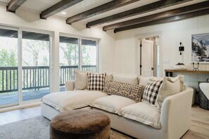 A cozy living room with a large sofa, a wooden bench, and a view of the outdoors through large sliding doors. - @grizzlymountainhouse-lake access/firepit/games (Lake Arrowhead)