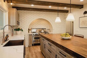 A kitchen with a brick wall, wooden ceiling beams, a central island, and pendant lighting. - @grizzlymountainhouse-lake access/firepit/games (Lake Arrowhead)