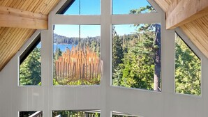 Una habitación con ventanas amplias, techo de madera y vista a un bosque y un lago.