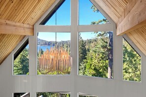 A room with large windows, a wooden ceiling, and a view of a forest and lake. - The Lakeview House (w/ hot tub, by @To_Dwell_Here) (Lake Arrowhead)